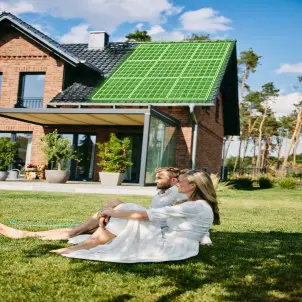 Eine Paar sitzt auf einer Wiese, im Hintergrund ist ein Haus, auf dessen Dach eine Photovoltaikanlage angedeutet ist
