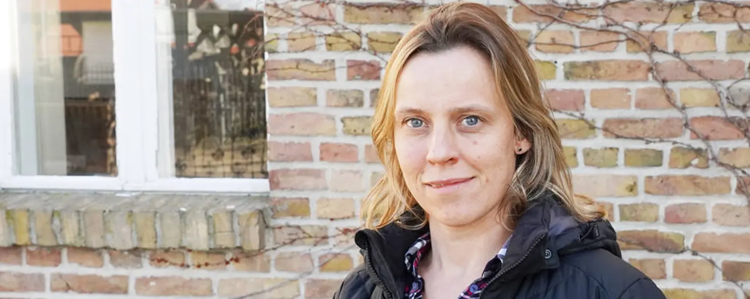 Eine Frau steht vor einem Backstein-Gebäude und lächelt in die Kamera