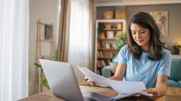 Erwachsene Frau analysiert Papiere vor ihrem Laptop